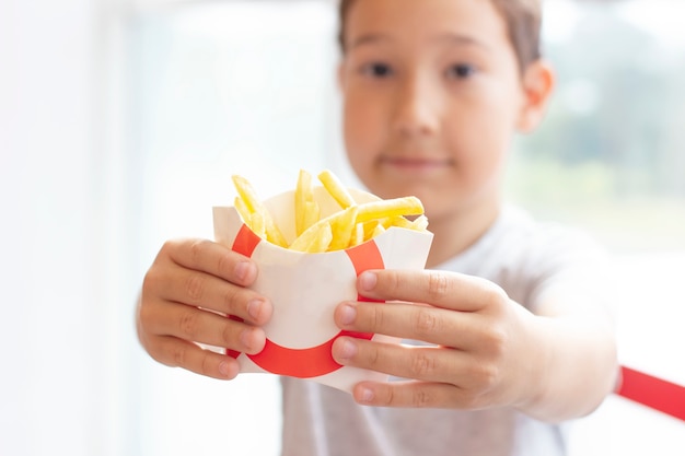 Il ragazzo di 8 anni porge le patatine in scatola di carta, concetto di fast food