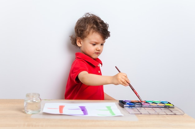 Il ragazzo dipinge al tavolo con i colori su un pezzo di carta.