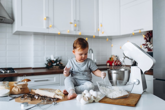 Il ragazzo divertente della famiglia felice che prepara la pasta, cuoce i biscotti nella cucina