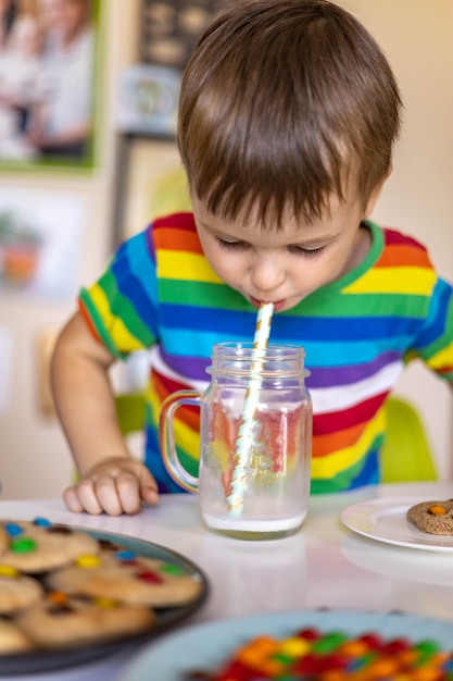 Il ragazzo divertente mangia i biscotti con i dolci multicolori rotondi mm e beve il latte