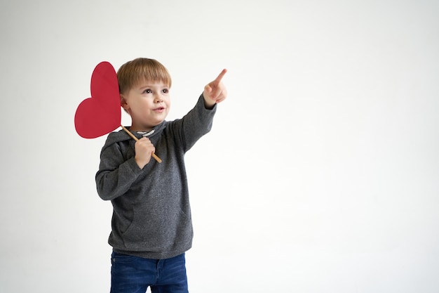 Il ragazzo dolce che tiene il cuore di carta rosso su fondo bianco scherza il concetto medico di sanità