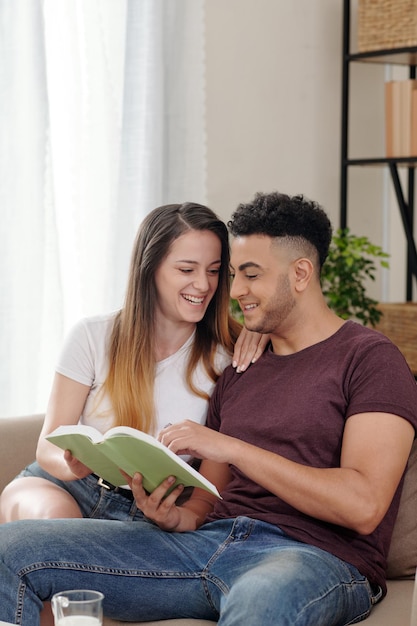 Il ragazzo e la ragazza che ridono leggono insieme un libro divertente quando trascorrono un weekend romantico a casa