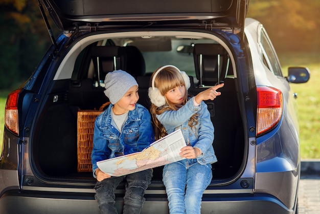 Il ragazzo e la ragazza piacevoli stanno guardando la road map mentre erano seduti nel bagagliaio dell'auto e discutevano della direzione di movimento. Viaggio di vacanza in famiglia in auto.