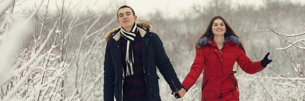 Il ragazzo e la ragazza si riposano nei boschi d'inverno Marito e moglie nella neve Giovane coppia che cammina nel parco invernale