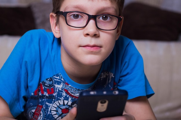 Il ragazzo è sdraiato sul pavimento con in mano uno smartphone e guardando la telecamera