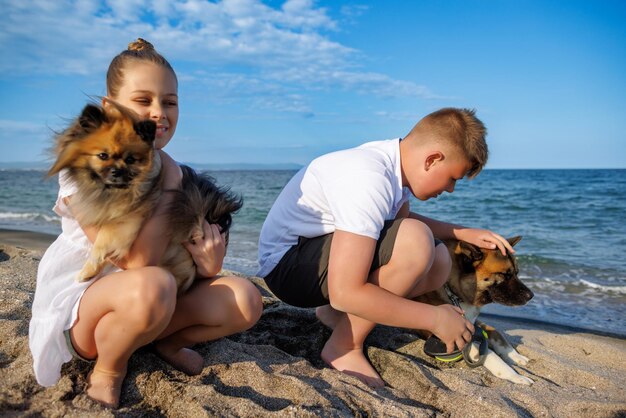 Il ragazzo e sua sorella in abiti leggeri camminano e si rilassano con i cani Pomerania e Akita Inu sulla spiaggia lungo il Mar Nero