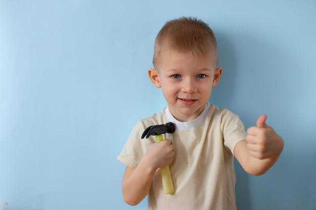 Il ragazzo è un piccolo costruttore con un martello in mano su sfondo blu in studio