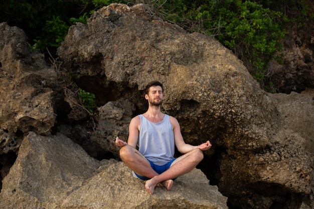 Il ragazzo fa yoga sugli scogli