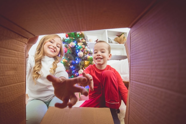 Il ragazzo felice e una ragazza aprono la scatola sullo sfondo dell'albero di natale