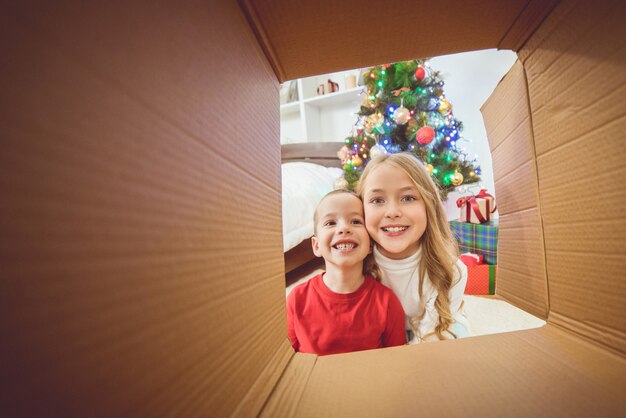 Il ragazzo felice e una ragazza aprono la scatola vicino all'albero di Natale