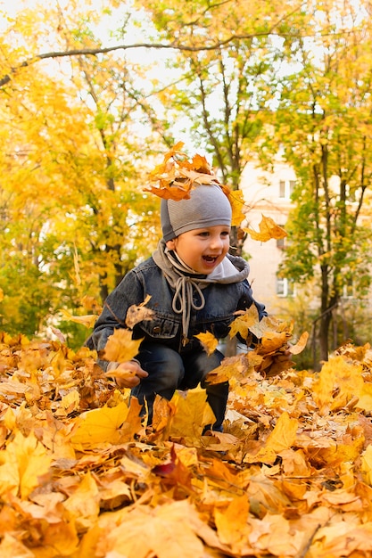 Il ragazzo felice gioca nel fogliame di autunno