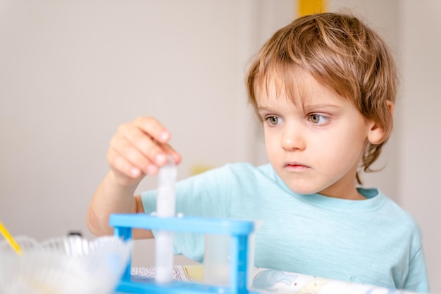 Il ragazzo felice in maglietta blu conduce esperimenti chimici con aceto e soda a casa. il concetto di educazione domestica