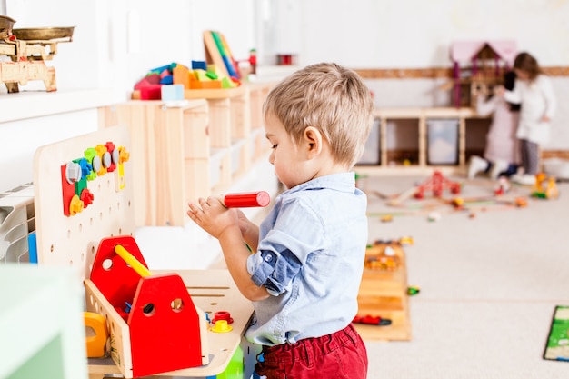 Il ragazzo gioca con gli strumenti di legno del costruttore nell'asilo