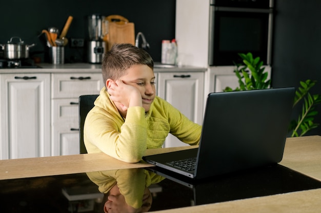 Il ragazzo in abiti gialli sta guardando un film studiando o giocando online sul computer nella cucina di casa