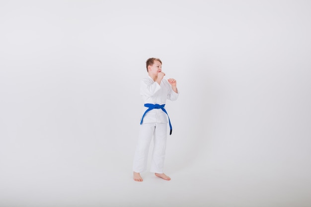 Il ragazzo in un kimono bianco con una cintura blu sta lateralmente in una posa su un muro bianco