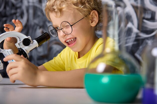 Il ragazzo in una maglietta gialla guarda i cristalli sul palco del microscopio in laboratorio