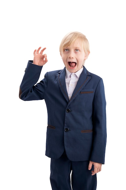 Il ragazzo in uniforme scolastica mostra un gesto OK e fa una faccia buffa Scolaro che scherza isolato su sfondo bianco