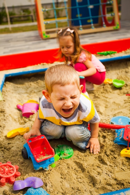 Il ragazzo infelice piangente gioca con l'auto nella sandbox al parco giochi