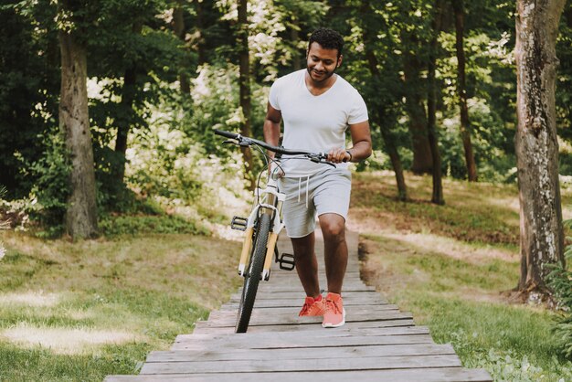 Il ragazzo latino sta rotolando la bici sul passaggio pedonale di legno.