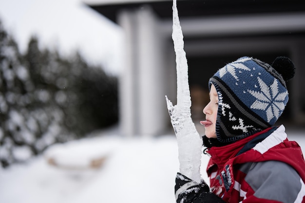 Il ragazzo lecca un ghiacciolo di ghiaccio con la lingua in inverno