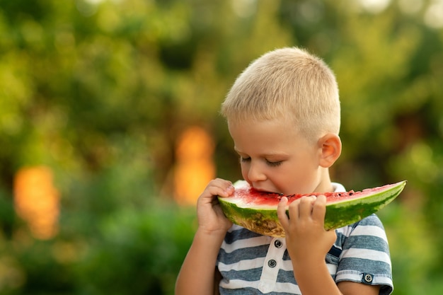 Il ragazzo mangia l'anguria all'aperto. vacanze estive in campagna.