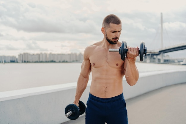 Il ragazzo muscoloso esercita i muscoli dei treni senza camicia all'aperto motivati per il fitness Concetto di bodybuilding sportivo