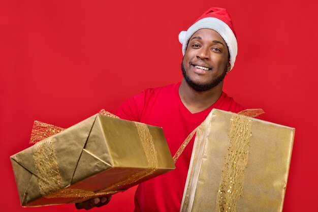 Il ragazzo nero con un sorriso a trentadue denti con un cappello da Babbo Natale fa un regalo di Natale in un pacchetto dorato