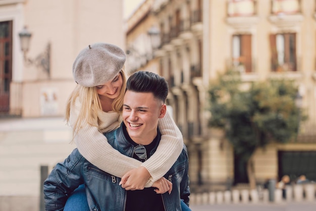 Il ragazzo porta la sua ragazza sulla schiena che ride in città