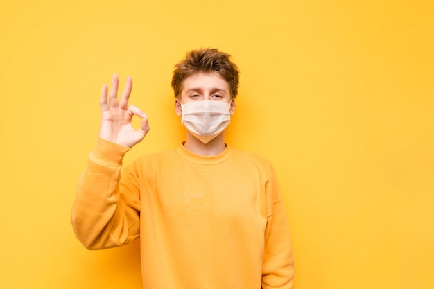Il ragazzo positivo con una maschera medica isolata su uno sfondo giallo guarda la telecamera