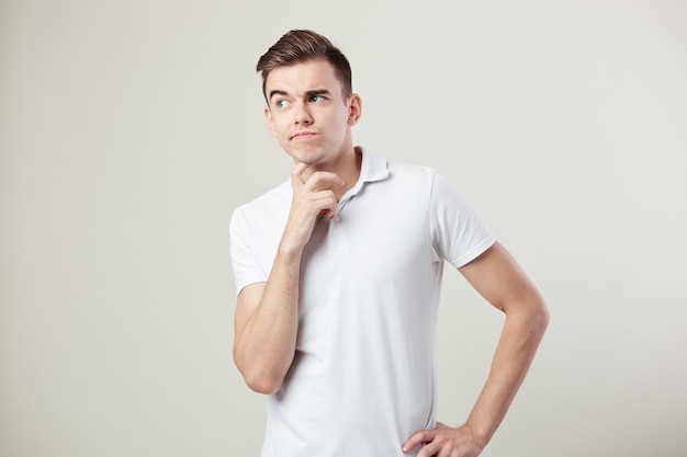 Il ragazzo premuroso vestito con una maglietta bianca e jeans è su uno sfondo bianco in studio.