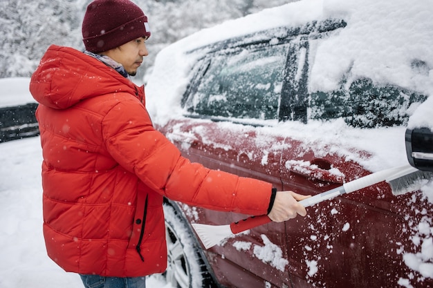 Il ragazzo pulisce l'auto dalla neve con una spazzola