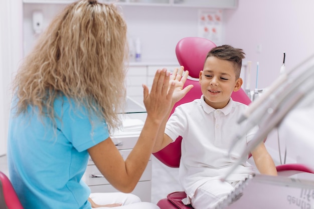 Il ragazzo ride e fa una mano di rispetto con una donna dentista dopo una visita e un esame in odontoiatria