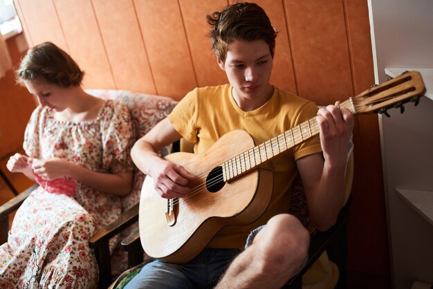 Il ragazzo seduto a suonare la chitarra con una ragazza che lavora a maglia il prodotto