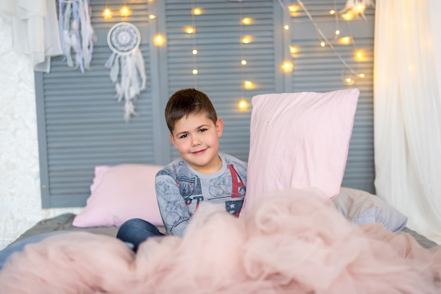 Il ragazzo seduto sul letto e con in mano un cuscino rosa nella stanza di Natale