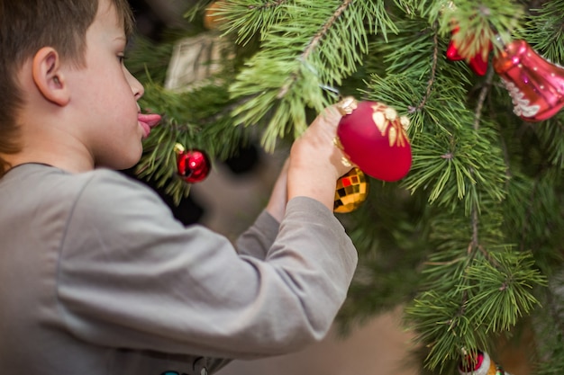 Il ragazzo si aggrappa a una palla rossa su un ramo di un albero di Natale a casa Preparandosi per il Natale a casa