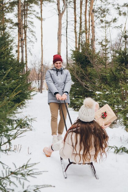 Il ragazzo si diverte a far slittare la sua ragazza con dei regali in una foresta di conifere invernale