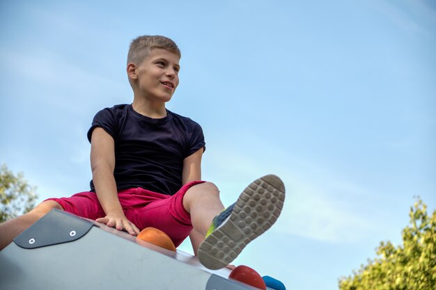 Il ragazzo si siede nel parco su una collina e guarda lontano contro il cielo blu. Copia spazio.