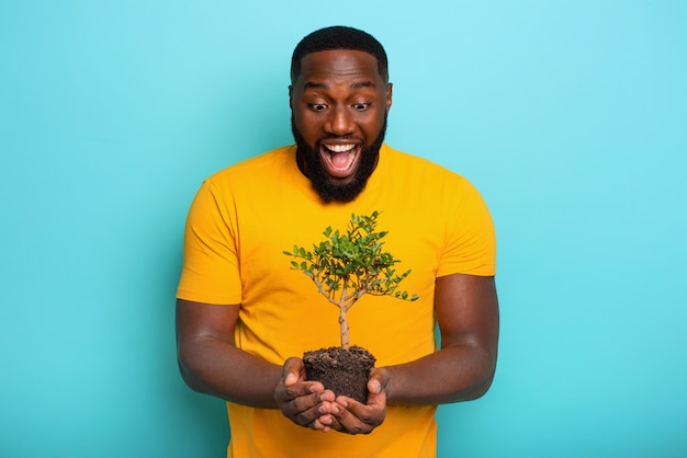 Il ragazzo sorpreso felice giudica un piccolo albero pronto per essere piantato. Concetto di forestazione