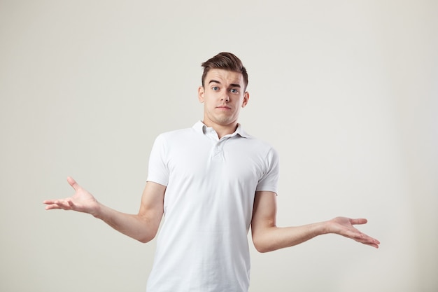 Il ragazzo sorpreso vestito con una maglietta bianca e jeans è su uno sfondo bianco in studio.