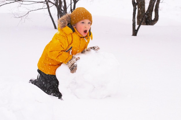 Il ragazzo sta facendo il pupazzo di neve nel parco