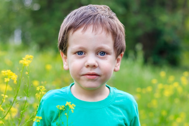 Il ragazzo sta nell'erba e nei fiori. Un ragazzo in una maglietta verde.