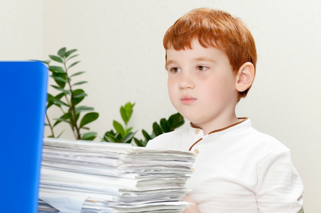 Il ragazzo stanco con i capelli rossi si siede con un gran numero di fogli di carta