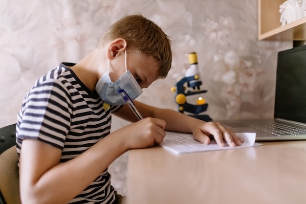 Il ragazzo studia a casa mentre indossa la maschera protettiva