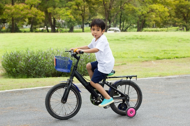 Il ragazzo sveglio asiatico guida una bicicletta al parco