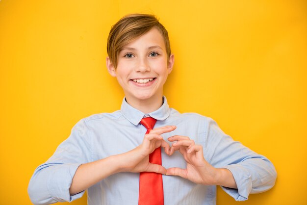 Il ragazzo teenager positivo sorridente mostra il cuore. San Valentino, amore e concetto creativo