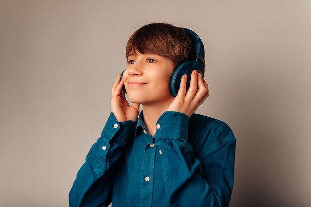 Il ragazzo teenager sognante sta tenendo le cuffie blu sulla sua testa che si gode la musica