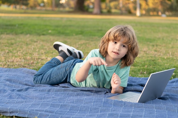 Il ragazzo teenager usa il computer portatile. istruzione in linea. di nuovo a scuola. comunicazione moderna. controllare la posta elettronica. studio del bambino in linea. ragazzo rilassarsi sull'erba del parco. digitando il blog della scuola sul computer. ragazzino in videolezione.