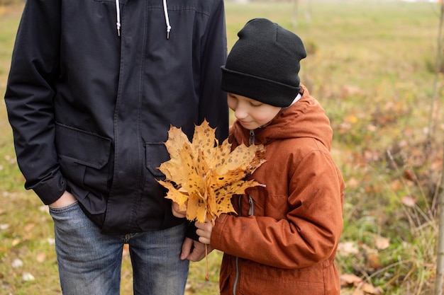 Il ragazzo tiene in mano un mazzo di foglie autunnali e la mano di suo padre