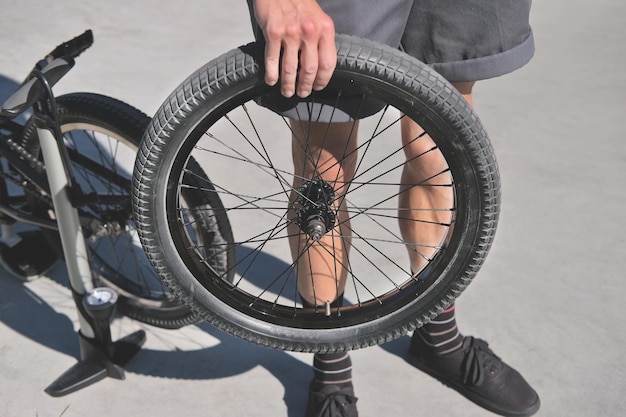 il ragazzo tiene in mano una ruota di bicicletta bmx sullo sfondo di una pompa e di una bicicletta durante la riparazione