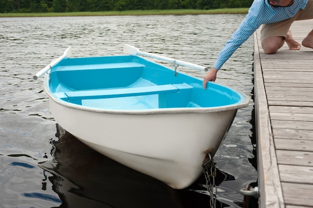 Il ragazzo tira la barca in piedi sull'acqua dal molo di legno con la mano.